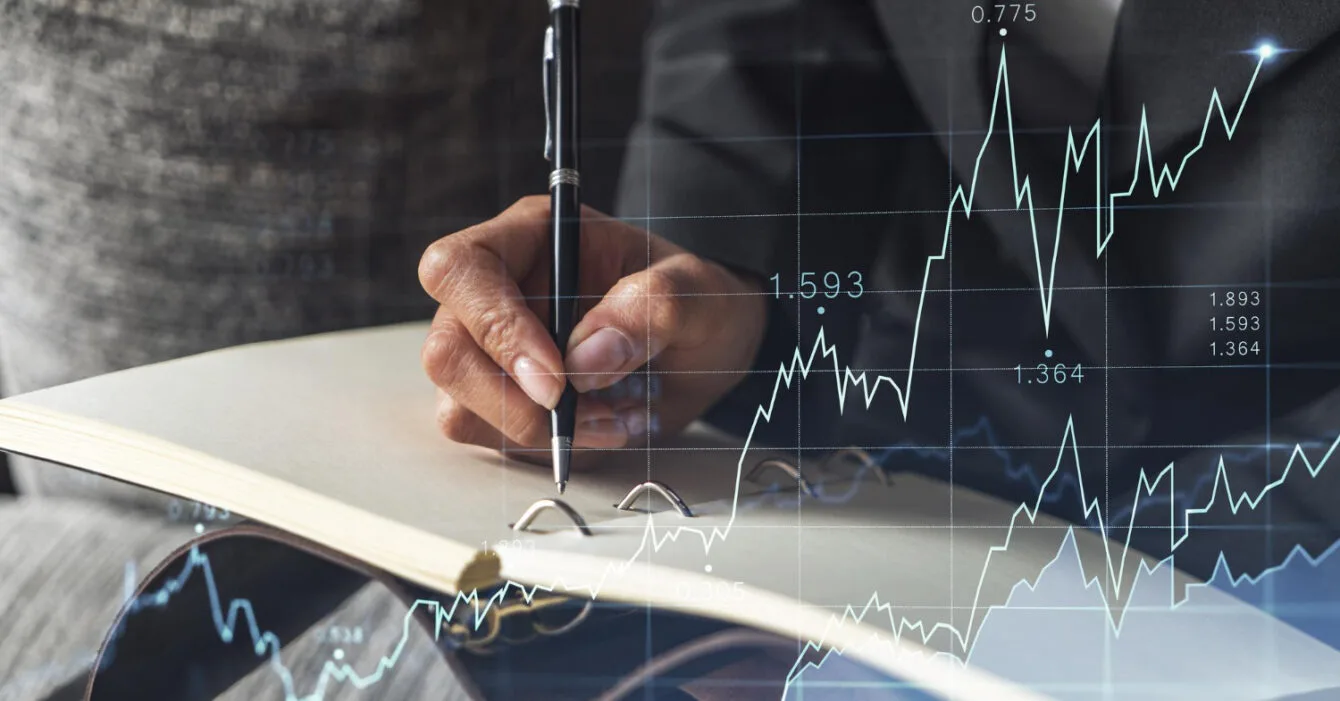 A person in a suit writing Asian M&A Investment Strategies in a notebook, overlaid with financial graphs and data, symbolizing investment and analysis.
