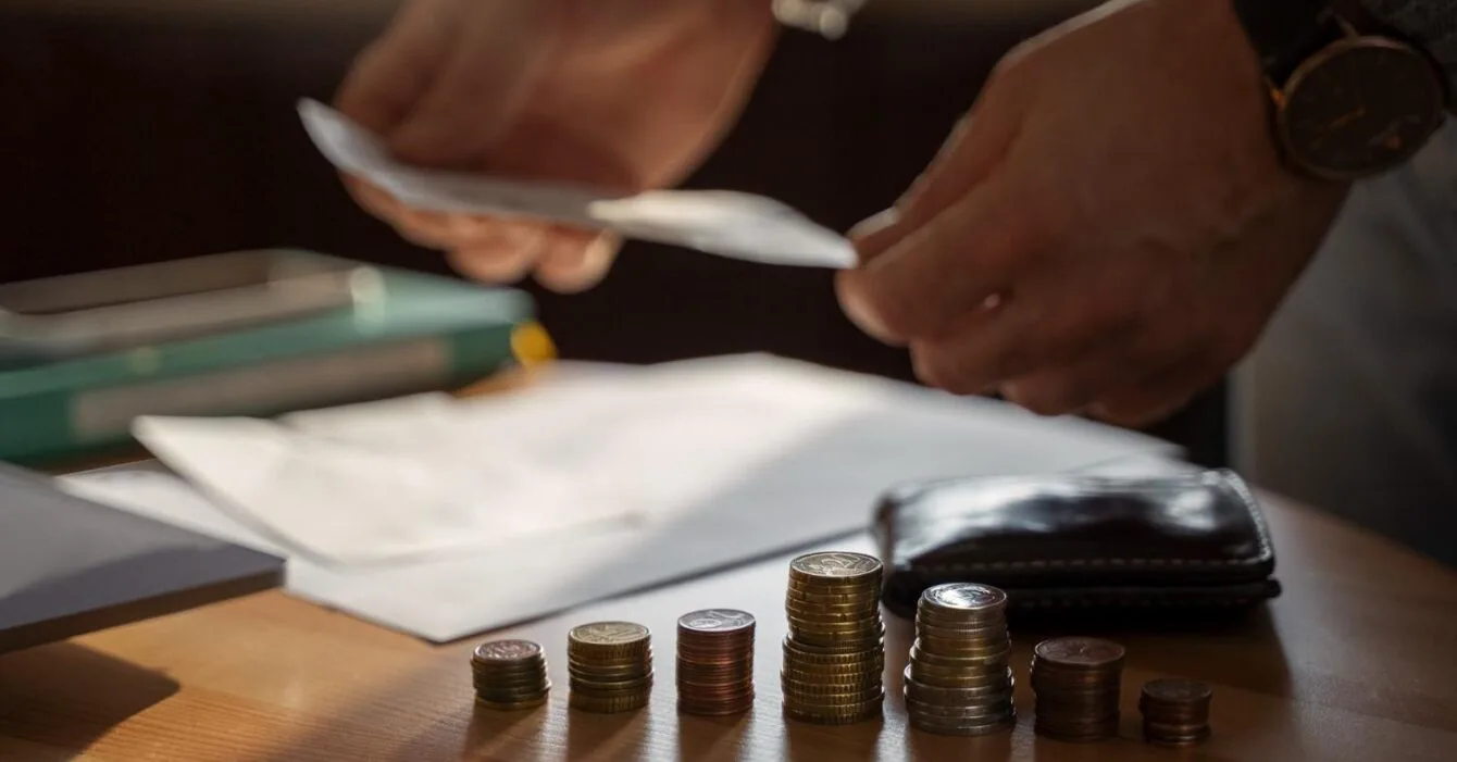 Asia M&A Private Equity Momentum: A person's hands sort bills while organizing stacked coins on a wooden table, with papers and a wallet visible in the background.