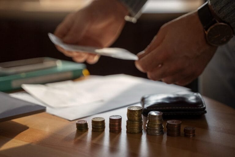 Asia M&A Private Equity Momentum: A person's hands sort bills while organizing stacked coins on a wooden table, with papers and a wallet visible in the background.