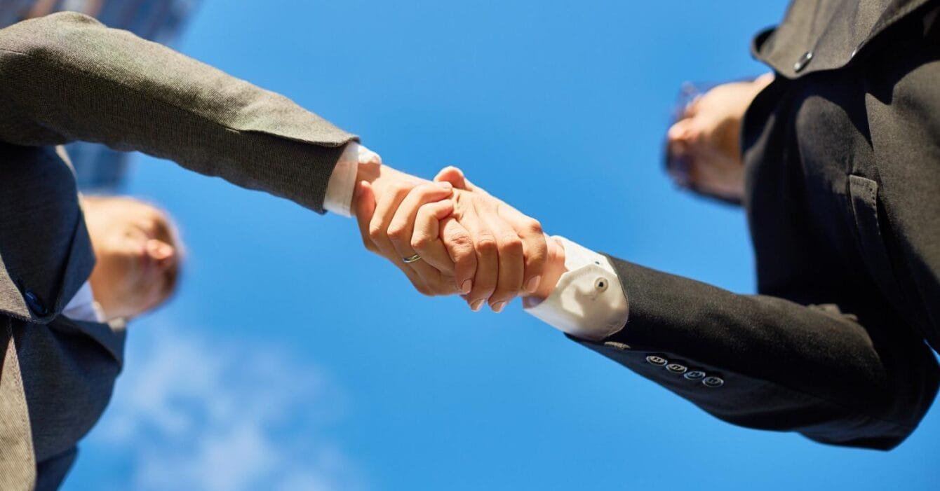 Asia Pacific M&A Resilience: Two business professionals shake hands under a clear blue sky, symbolizing partnership and agreement.