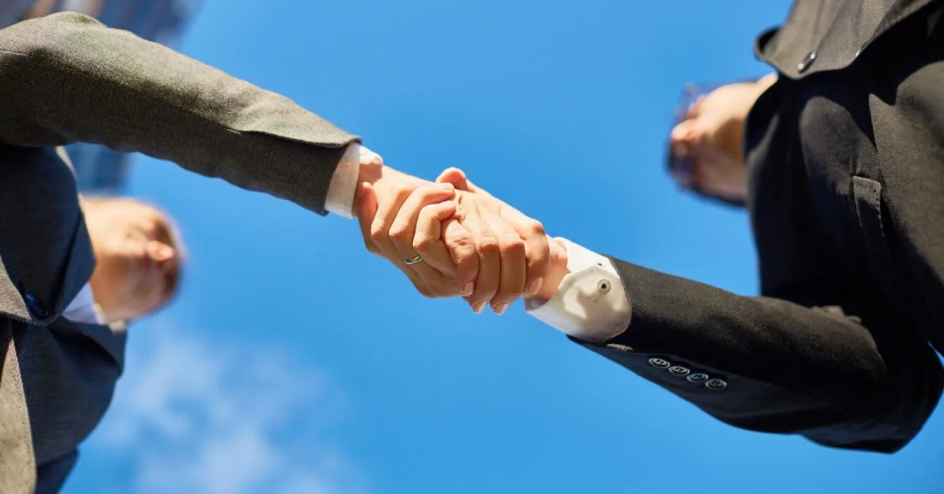 Asia Pacific M&A Resilience: Two business professionals shake hands under a clear blue sky, symbolizing partnership and agreement.