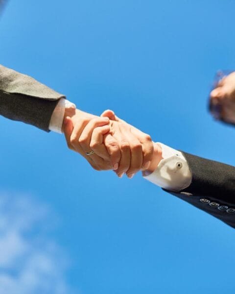 Asia Pacific M&A Resilience: Two business professionals shake hands under a clear blue sky, symbolizing partnership and agreement.