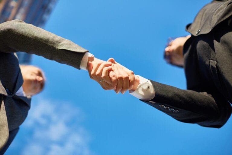 Asia Pacific M&A Resilience: Two business professionals shake hands under a clear blue sky, symbolizing partnership and agreement.