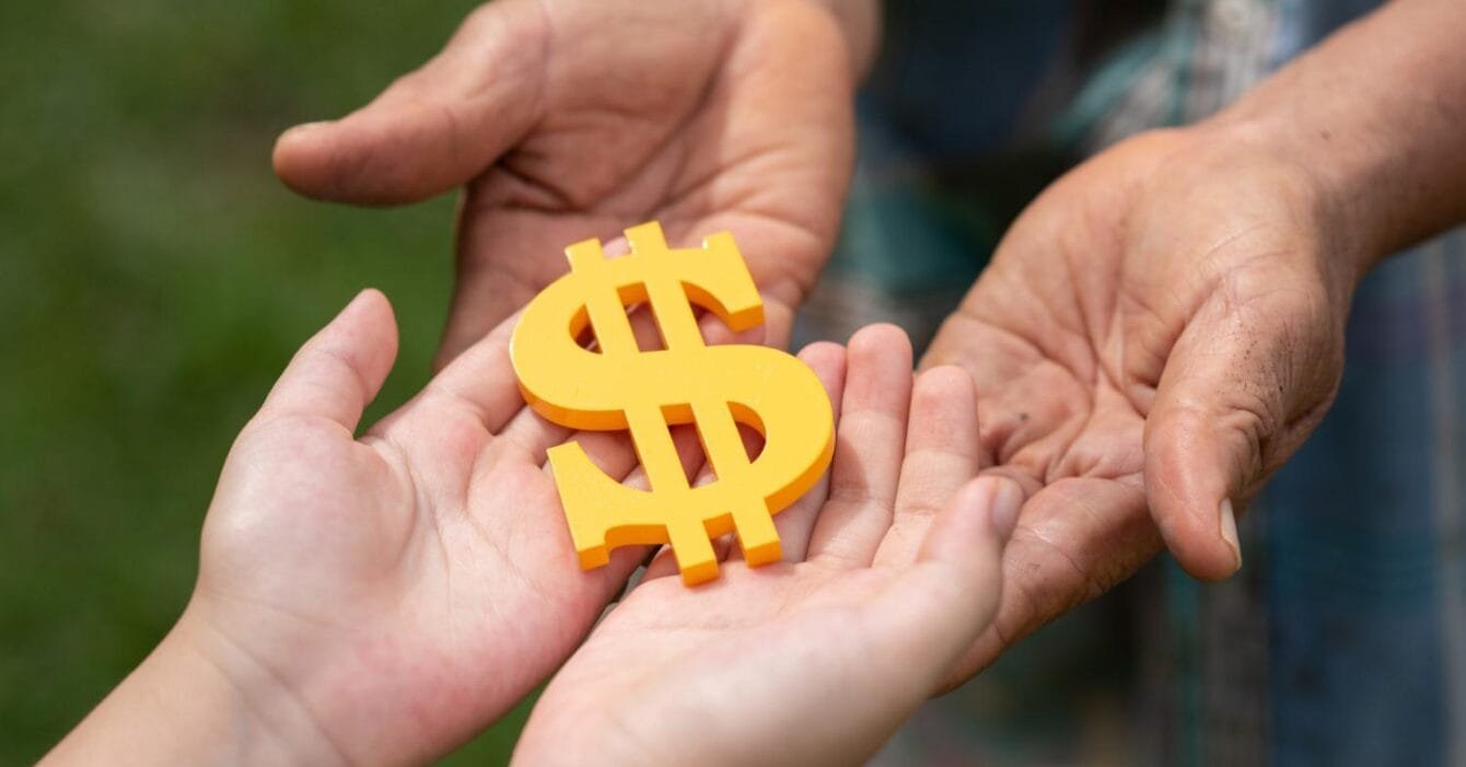 Asia Infrastructure M&A Fundraising: A child's hands receive a yellow dollar sign from an older adult's hands, symbolizing a transfer of wealth and support.