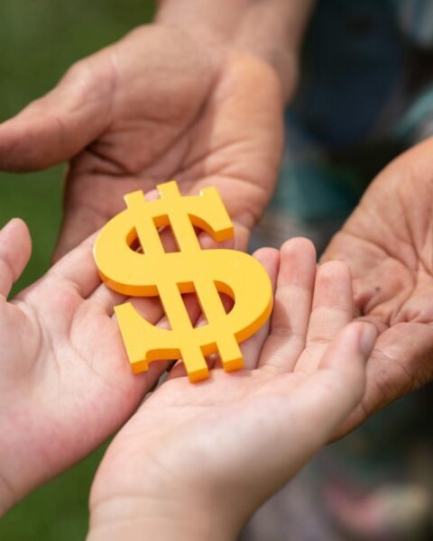 Asia Infrastructure M&A Fundraising: A child's hands receive a yellow dollar sign from an older adult's hands, symbolizing a transfer of wealth and support.