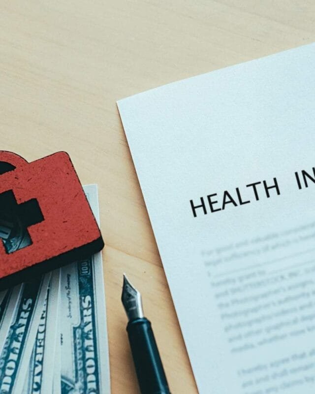 Asia M&A Insurance Trends: A red medical bag sits atop dollar bills next to a health insurance document and a fountain pen on a wooden surface.