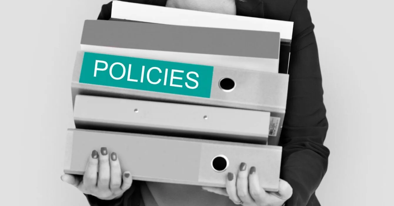 121481 Asia M&A Regulatory Delays: A woman in a blazer holds several binders labeled "POLICIES," symbolizing organization and management of policy documents.