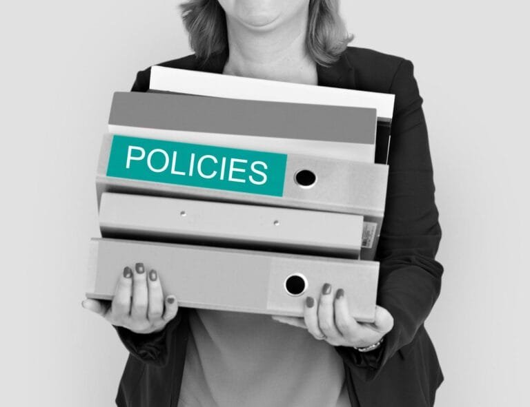 Asia M&A Regulatory Delays: A woman in a blazer holds several binders labeled "POLICIES," symbolizing organization and management of policy documents.