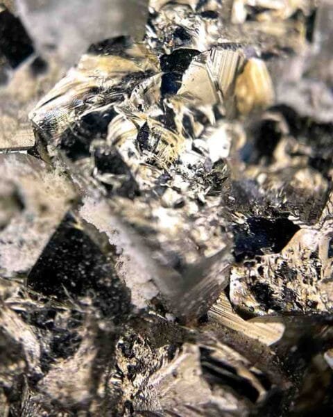 Asia M&A Rare-Earth Momentum: Close-up of reflective, jagged crystals, showcasing a mix of metallic silver and black hues with sharp angles and intricate textures.