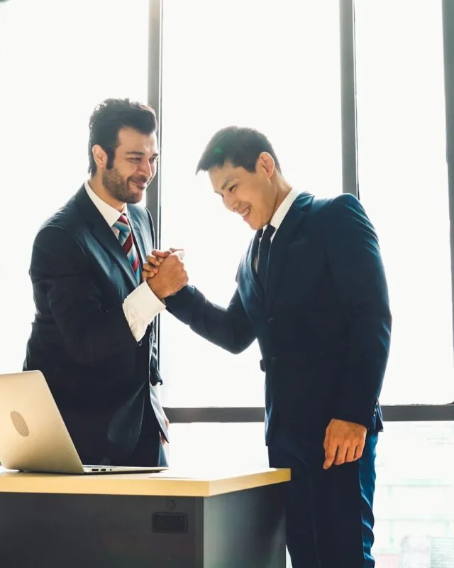 getty-images-2tor9SbDs_Q-unsplash Asia M&A Deal Value Growth: Two business professionals shake hands in front of a large window, with a laptop on the desk beside them, symbolizing a successful agreement.